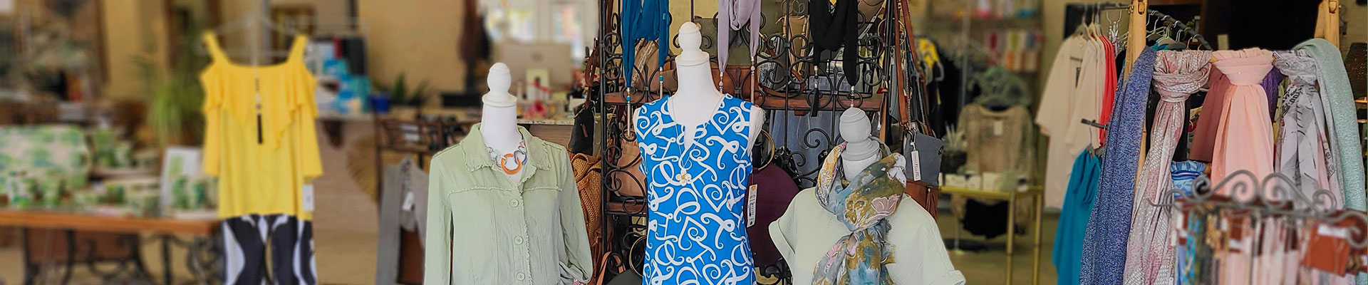 In a boutique, three mannequins wearing a dress, jacket, skirt and shawl