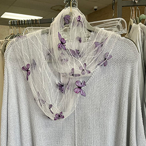 a beige sweater on the hanger draped with a gauzy scarf with butterfly motif