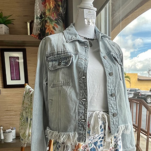 outfit on a mannequin consisting of a light wash jean jacket, a white shirt, floral pants, and earrings
